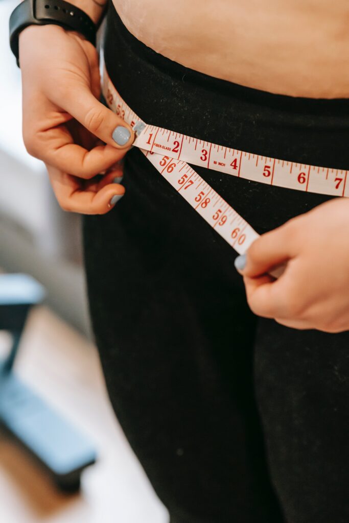 woman in black pants with tape measurer around her waist to measure waist circumference.